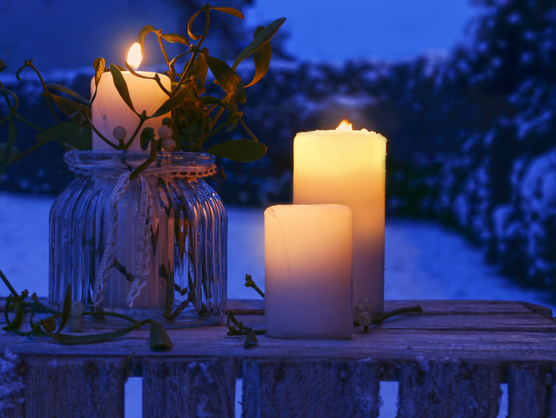 Candles decorated with mistletoe on rustic wooden table in winter garden
